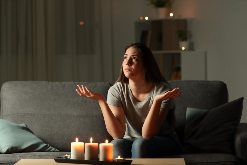 woman sitting on a couch in her living room with candles lit during a power outage