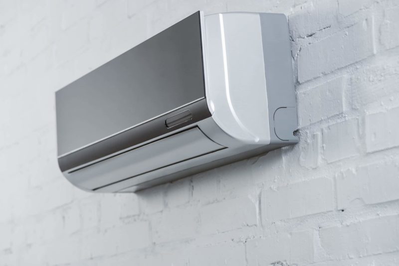 close-up shot of grey air conditioner hanging on white brick wall