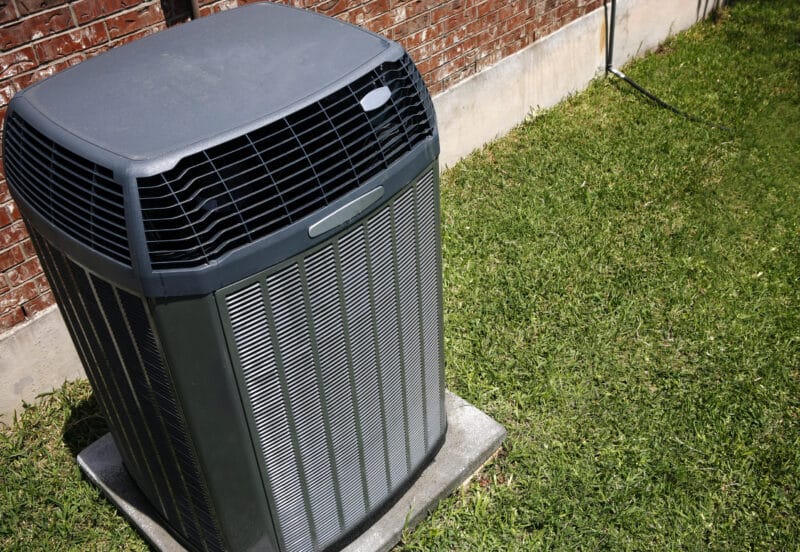 an outdoor ac unit on the grass next to a red brick home