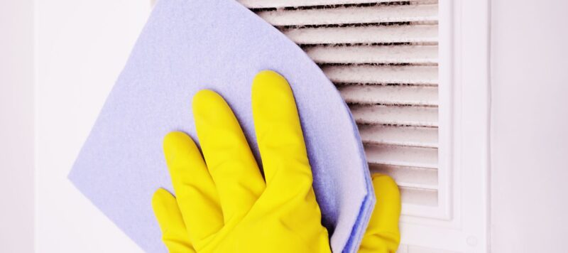 a gloved hand wiping down a dusty air vent
