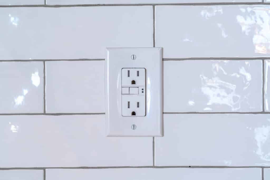 US outlet installed in a kitchen on white subway tile backsplash