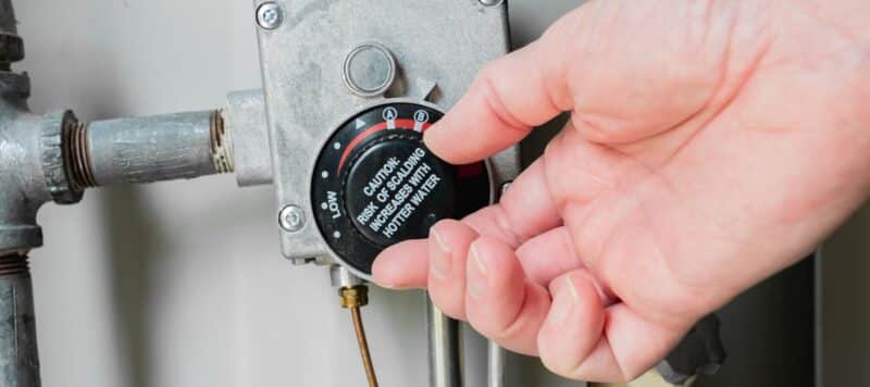 Hand adjusting the temperature dial on a water heater control